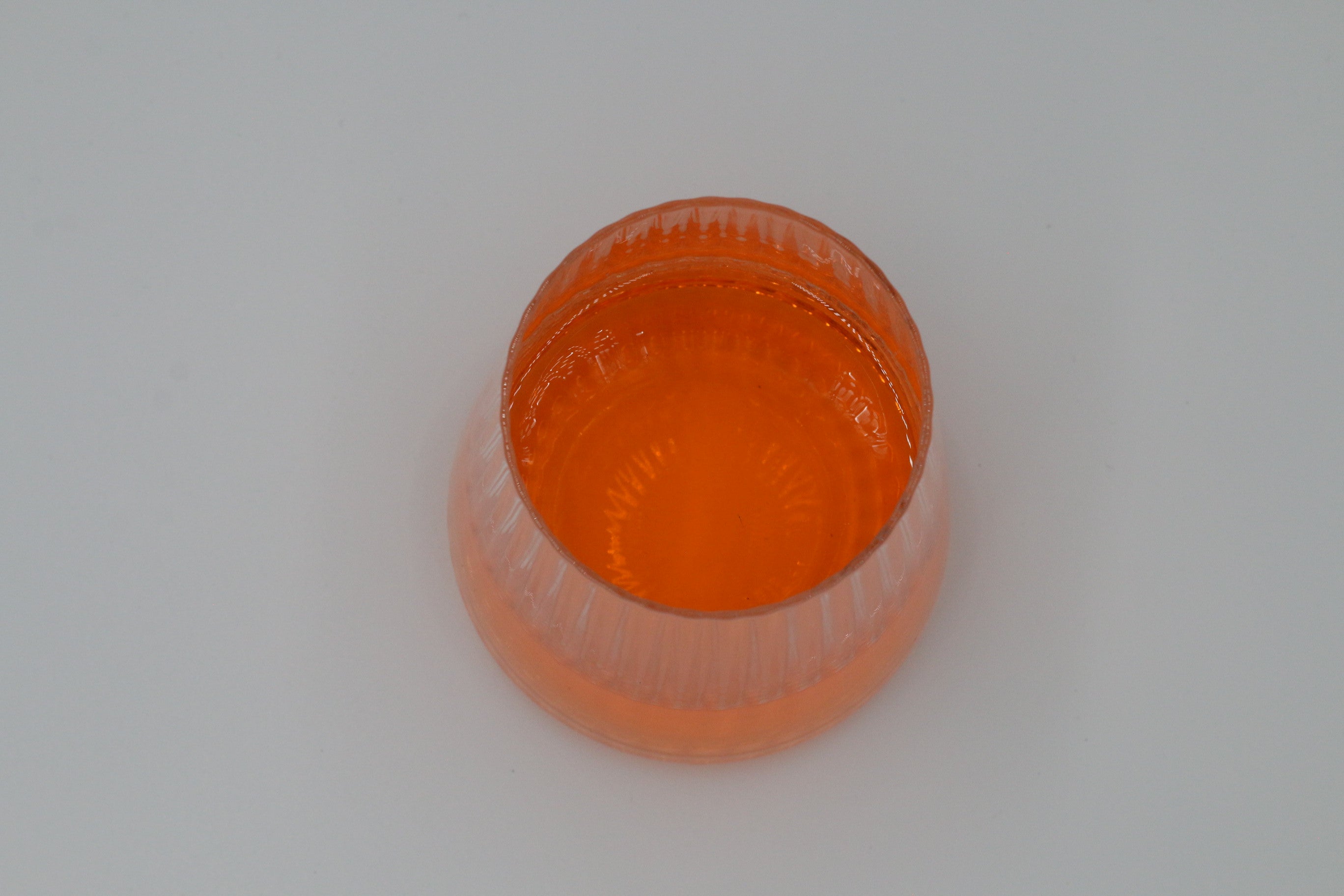 Geriffeltes Wasserglas in klein mit oranger Flüssigkeit.