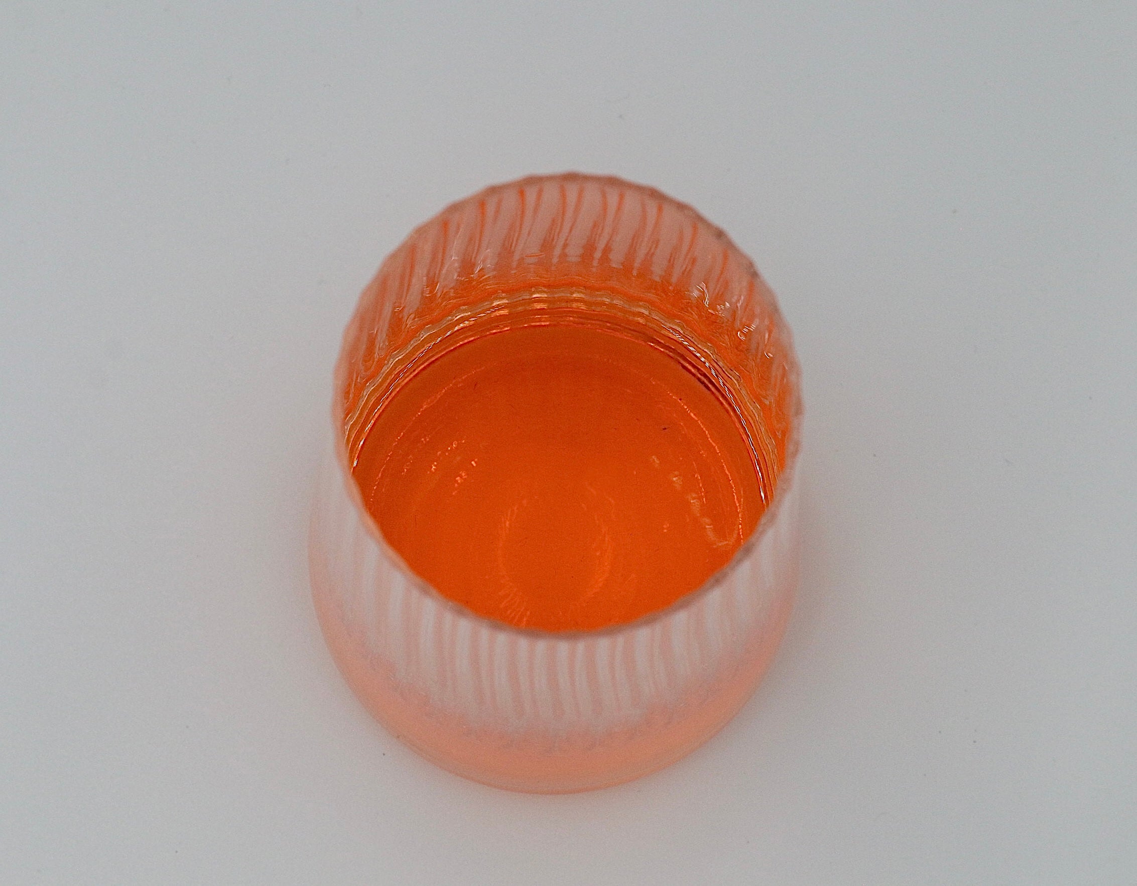 Geriffeltes Wasserglas in groß mit oranger Flüssigkeit.