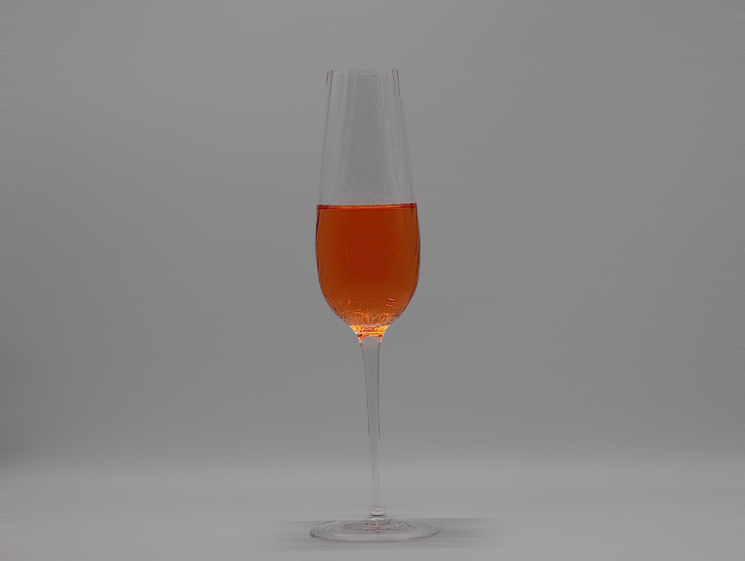 Gewelltes Sektglas mit oranger Flüssigkeit.