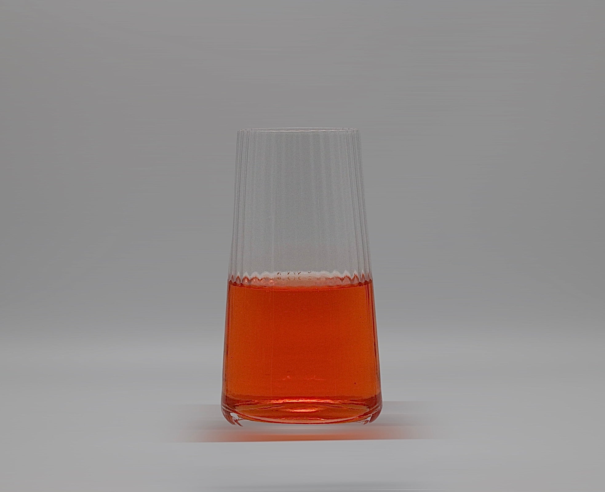 Geriffeltes Wasserglas in groß mit oranger Flüssigkeit.