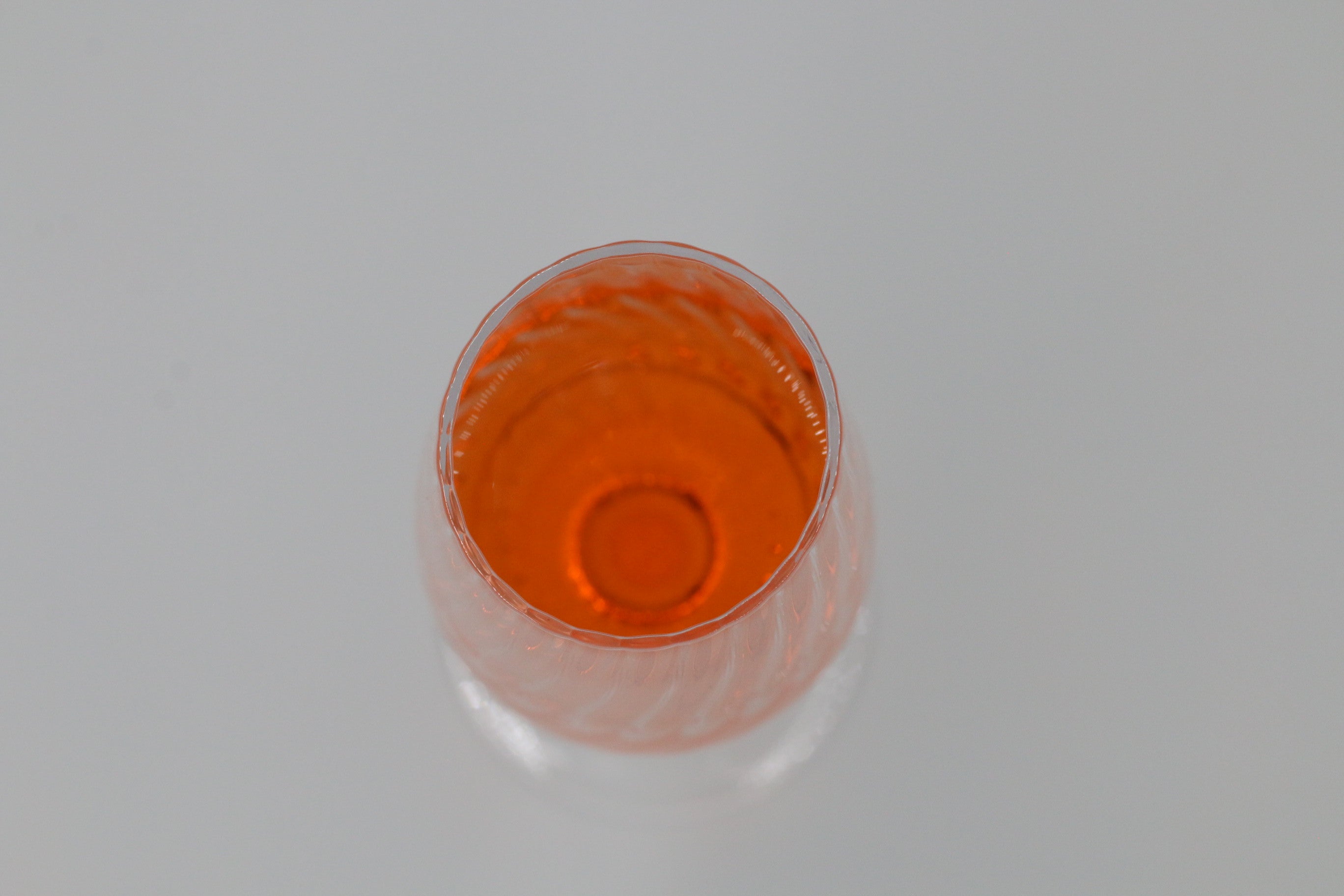 Gewelltes Sektglas mit oranger Flüssigkeit.