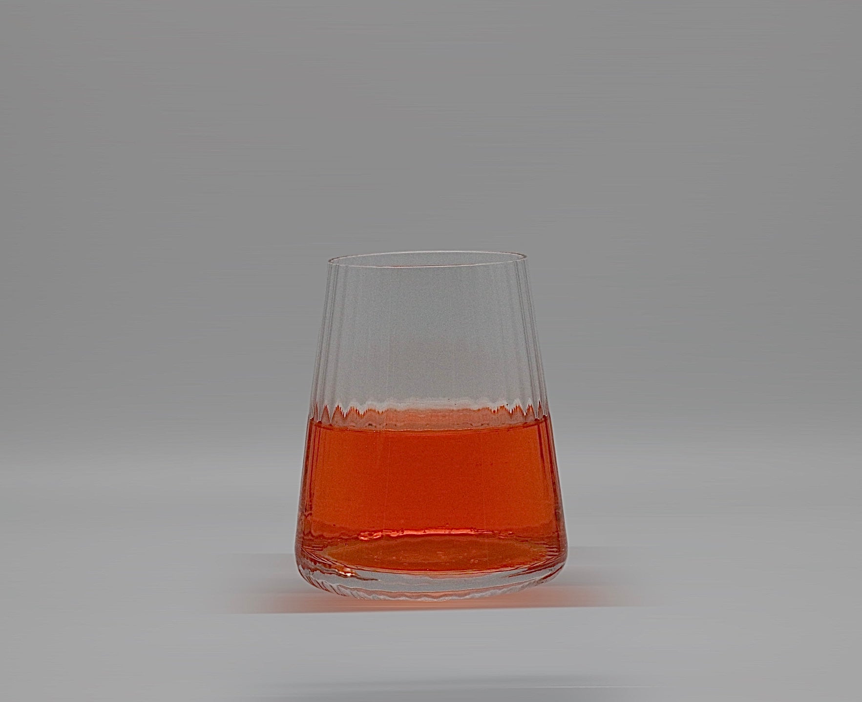 Geriffeltes Wasserglas in klein mit oranger Flüssigkeit.