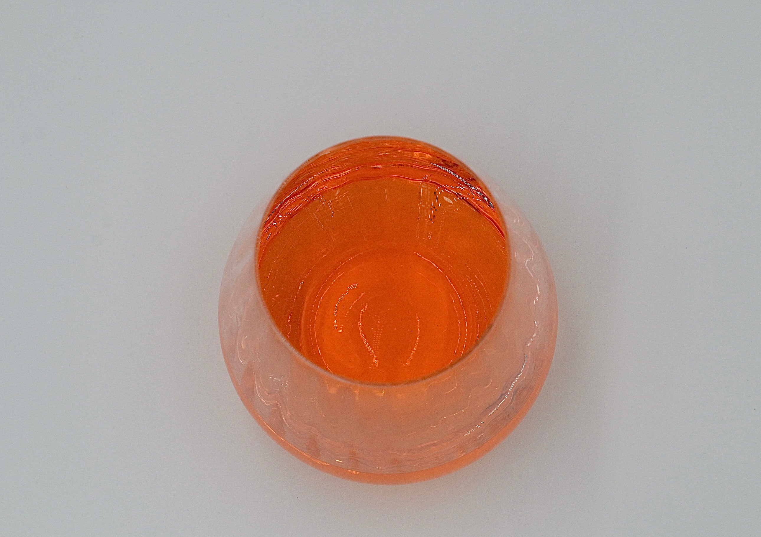 Wasserglas mit gewellter Struktur mit oranger Flüssigkeit.