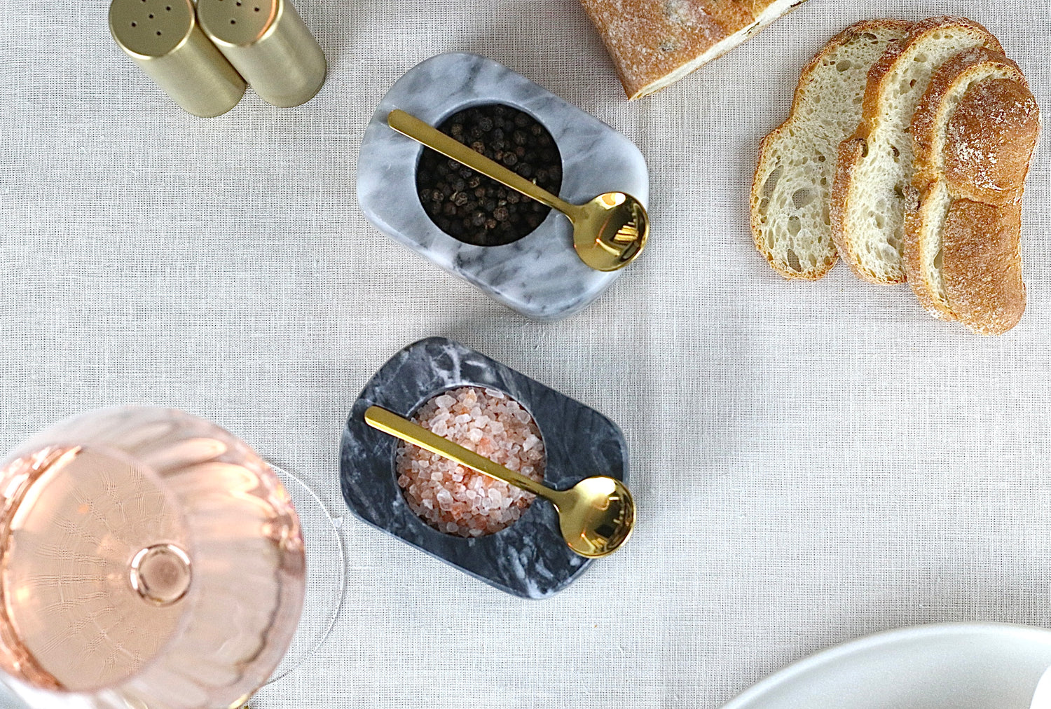 Offene Gewürzschale aus Marmor in Hellgrau oder Dunkelgrau mit goldenem Löffel, auf einem elegant gedeckten Tisch.