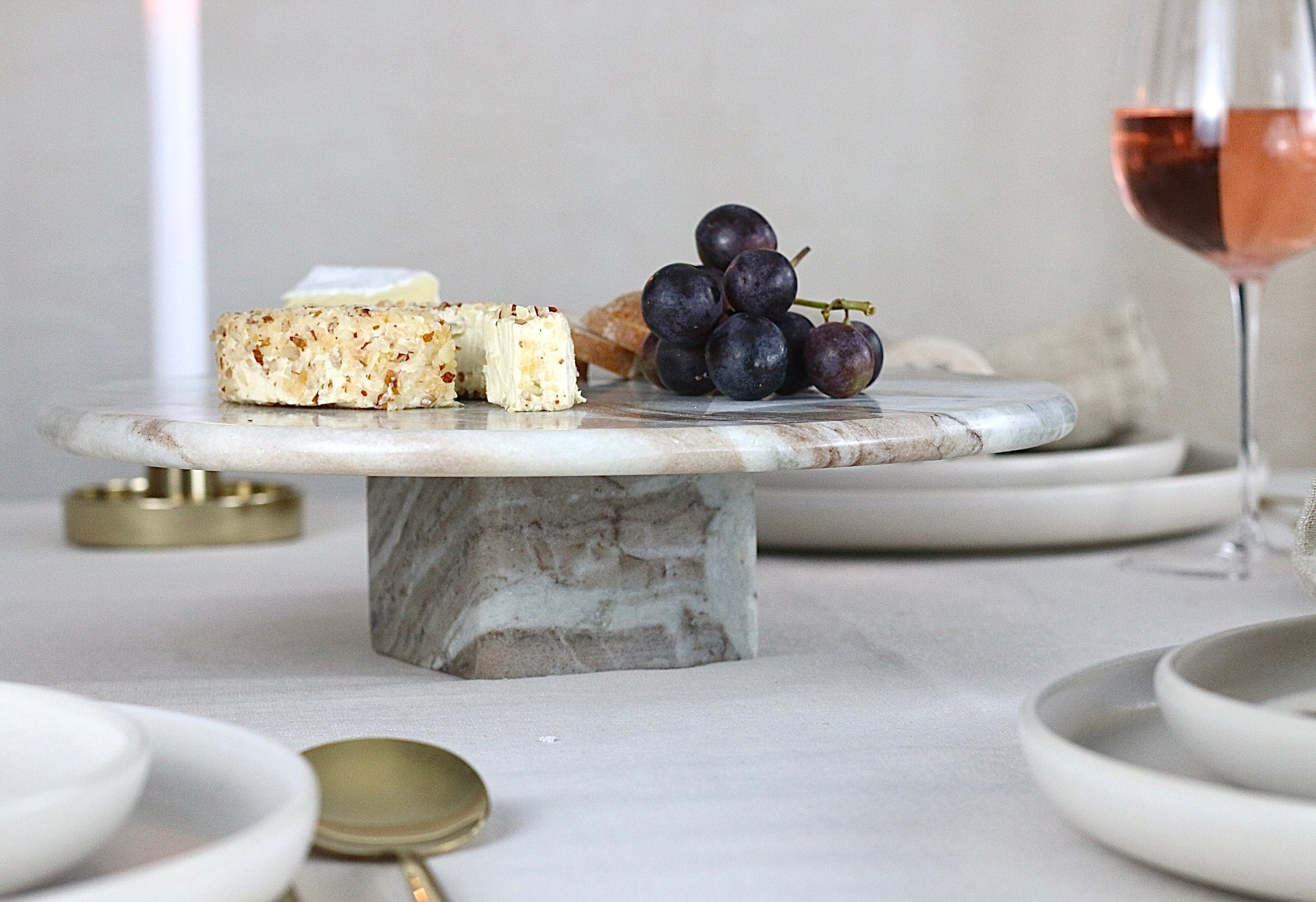 Marmor-Kuchenplatte mit quadratischem Marmorfuß in Beige, Grau und Braun, auf einem elegant gedeckten Tisch.