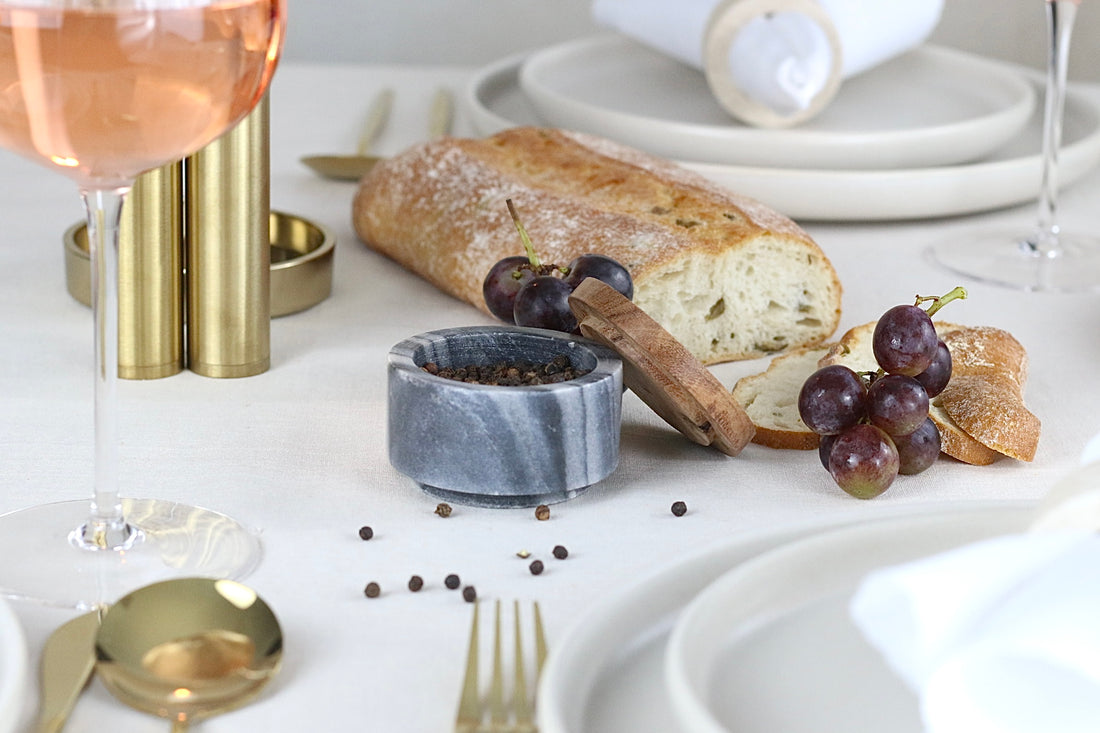 Kleine runde Gewürzschale aus dunkelgrau-weißem Marmor mit Holzdeckel, präsentiert auf einem elegant gedeckten Tisch.