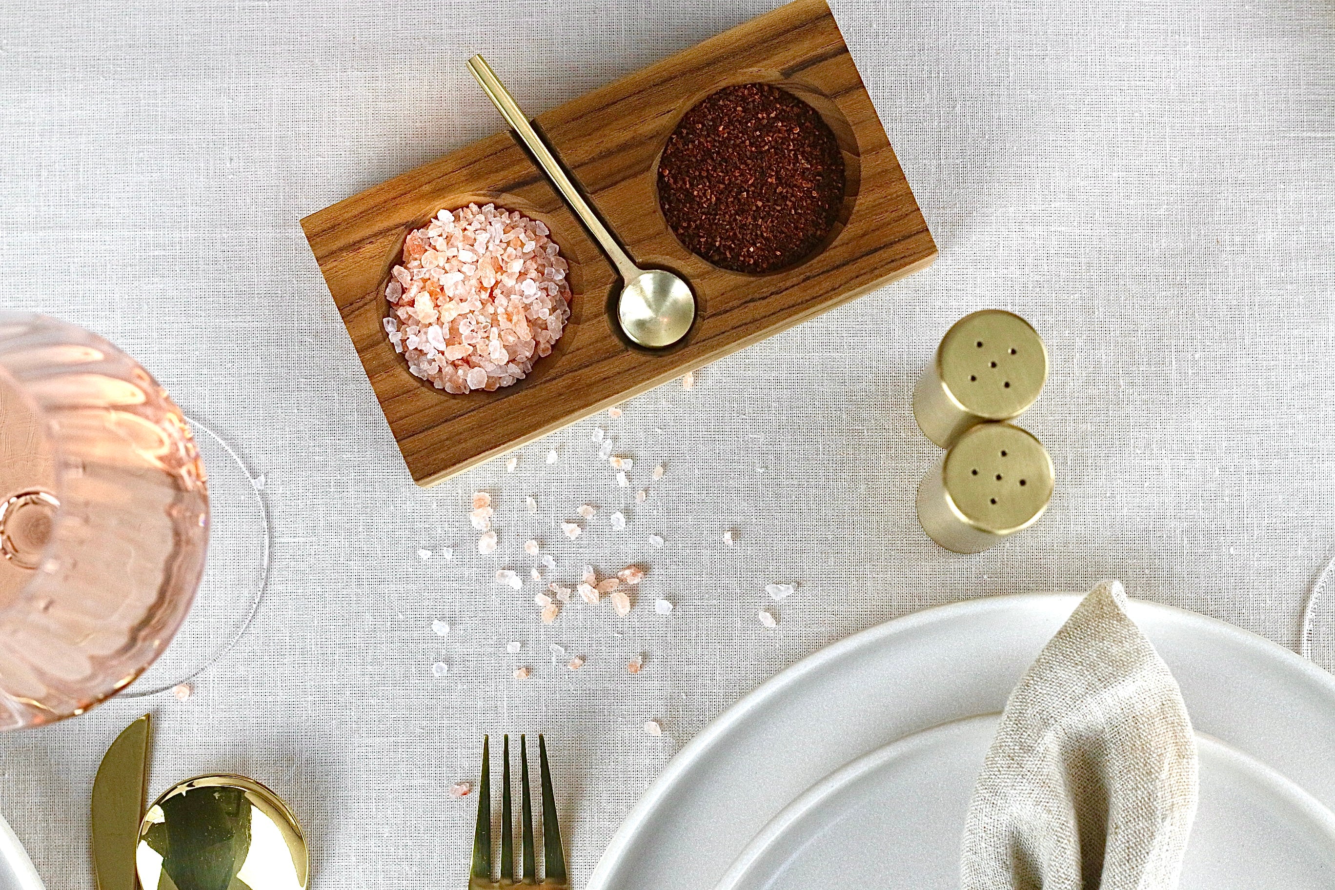 Gewürzschale aus Teakholz mit zwei Fächern und goldenem Löffel in Braun, auf einem elegant gedeckten Tisch.