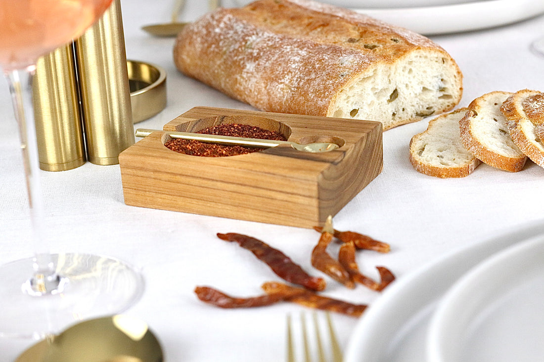 Gewürzschale aus Teakholz mit goldenem Löffel in Braun, auf einem elegant gedeckten Tisch.