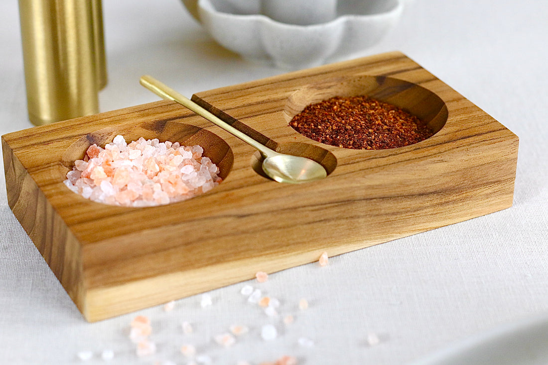 Gewürzschale aus Teakholz mit zwei Fächern und goldenem Löffel in Braun, auf einem elegant gedeckten Tisch.