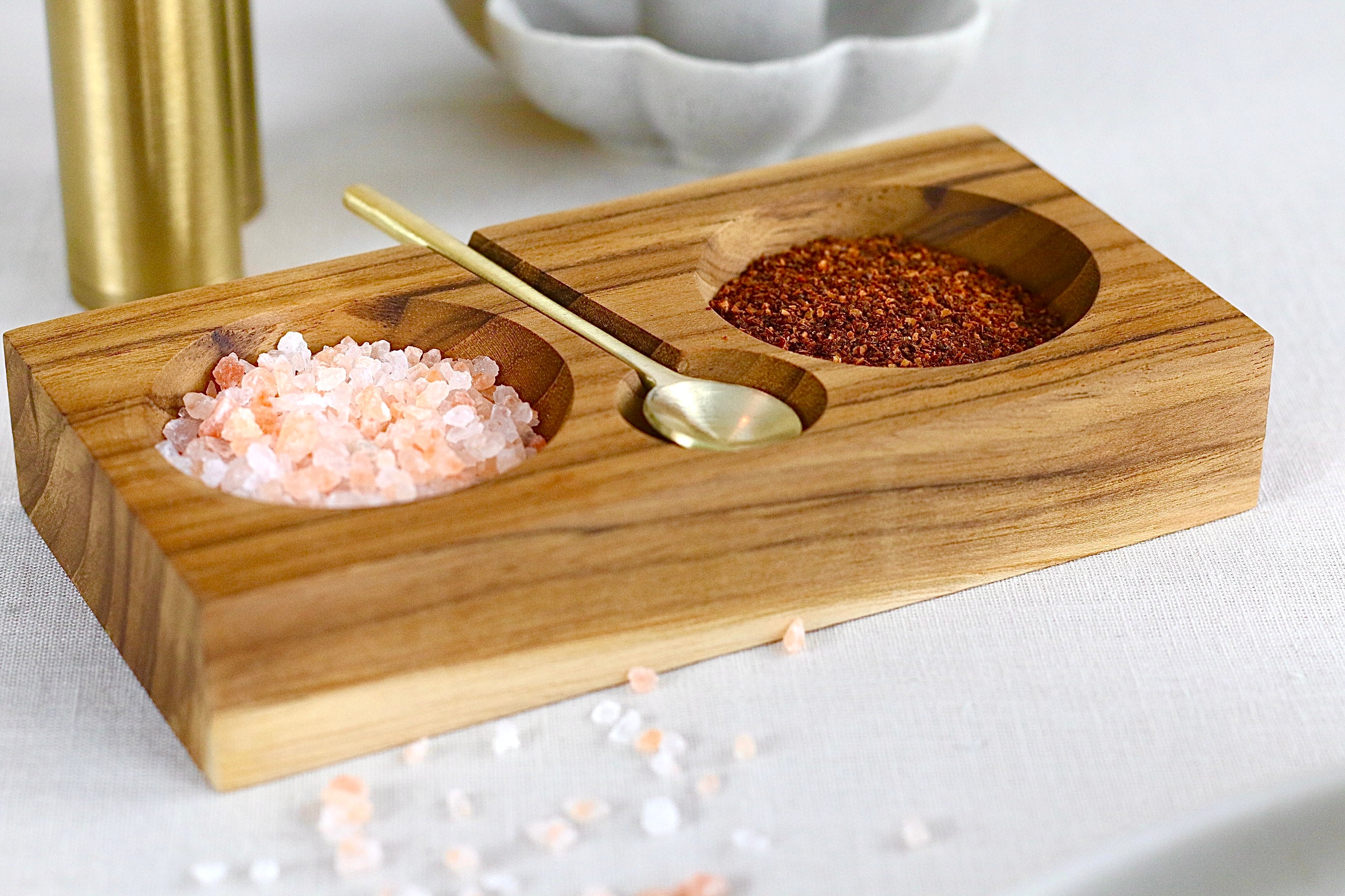 Gewürzschale aus Teakholz mit zwei Fächern und goldenem Löffel in Braun, auf einem elegant gedeckten Tisch.