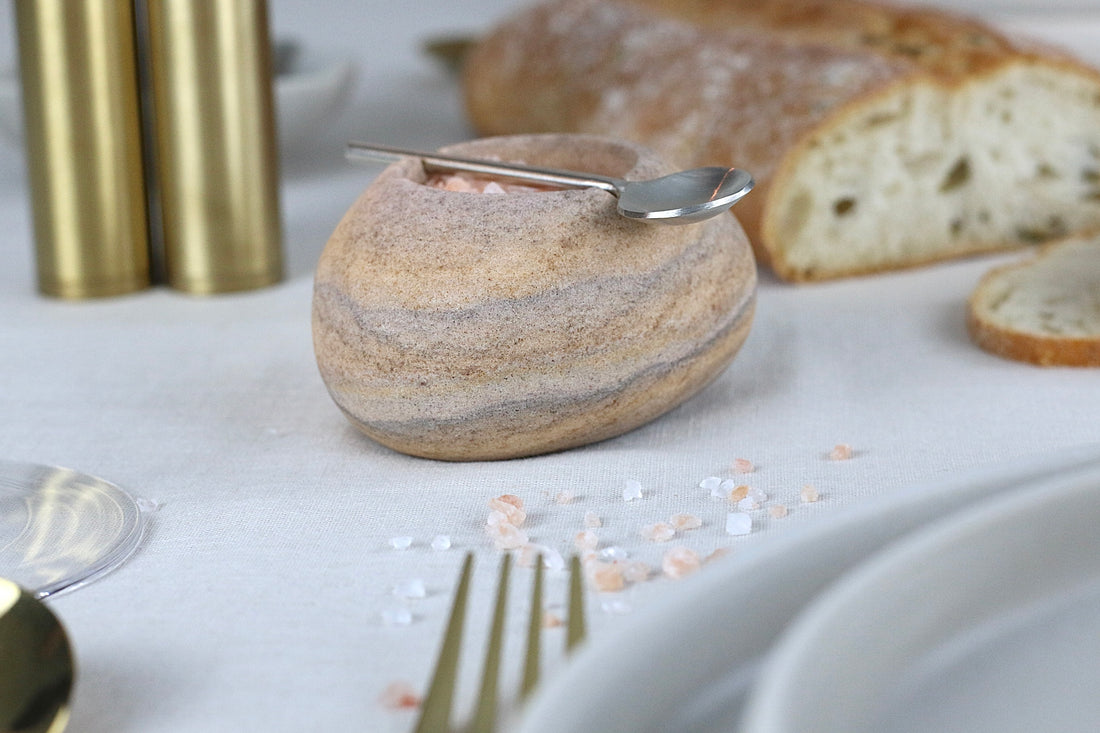 Beige-braun-grau marmorierte Gewürzschale aus Sandstein mit passendem Löffel, auf einem elegant gedeckten Tisch.