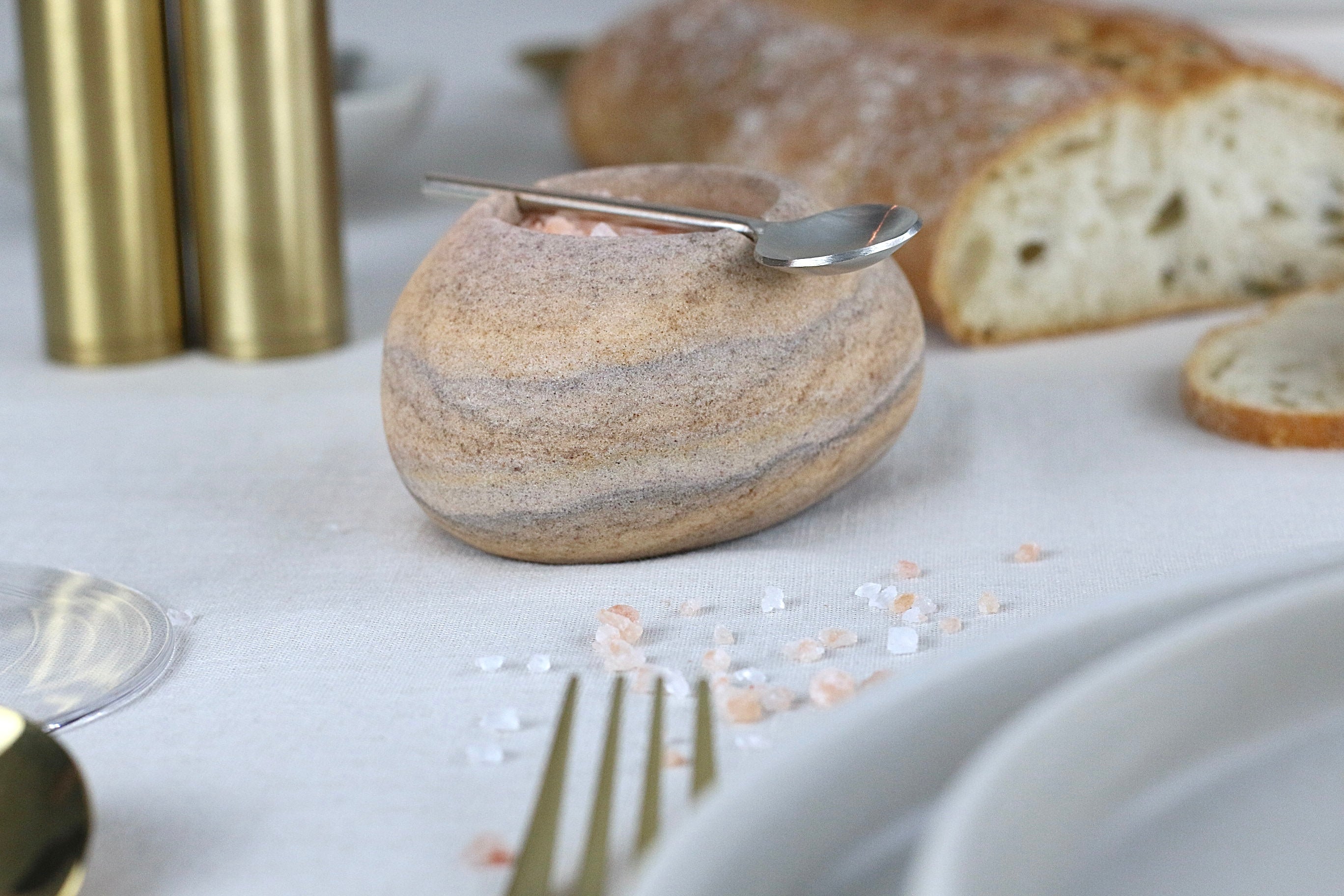 Beige-braun-grau marmorierte Gewürzschale aus Sandstein mit passendem Löffel, auf einem elegant gedeckten Tisch.